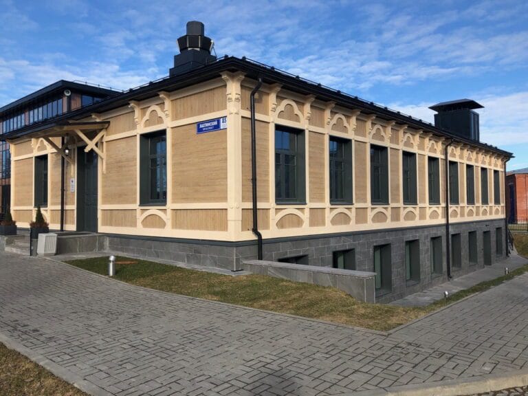 Воссоздание исторического облика утраченного деревянного здания для ресторана МФЦ Лахтинский 85. Реализован утепленный вентилируемый фасад с облицовкой под дерево из тонкого керамогранита, декоративными элементами из фибробетона и козырьками из клееной древесины. Компания «КровляФасадСистема» выполнила полный комплекс работ под ключ, включая сложный зимний монтаж.